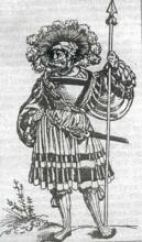 Landsknecht s krátkou kopijou a mečom "katzbalgerom", oblečený do barvitého dobového ošatenia, na ktorom zaujme hlavne bohato zdobený klobúk, pestrá sukňa a obrovské rukávy.